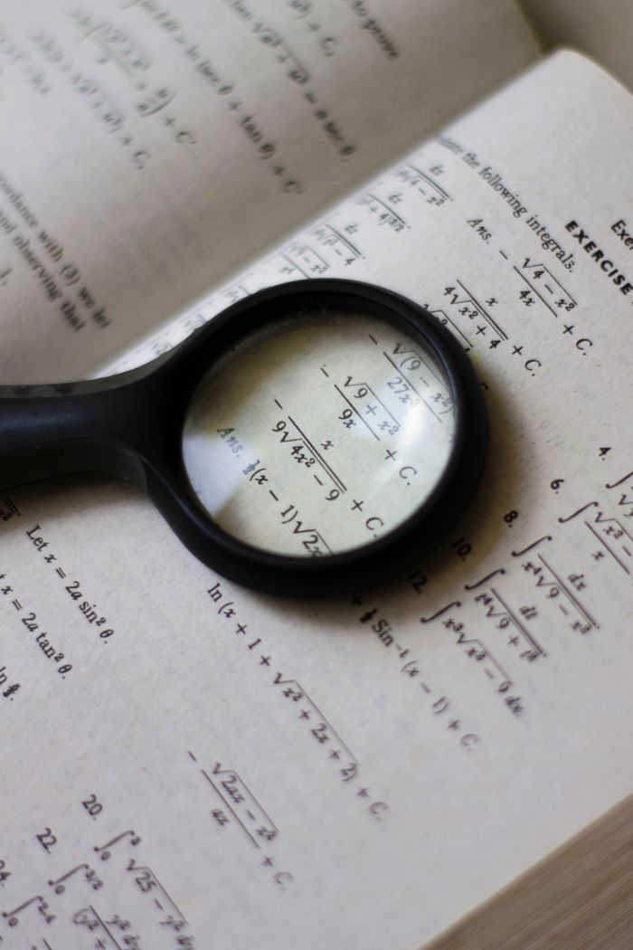 services-01 A magnifying glass focuses on mathematical equations in a textbook, highlighting detailed calculations.
