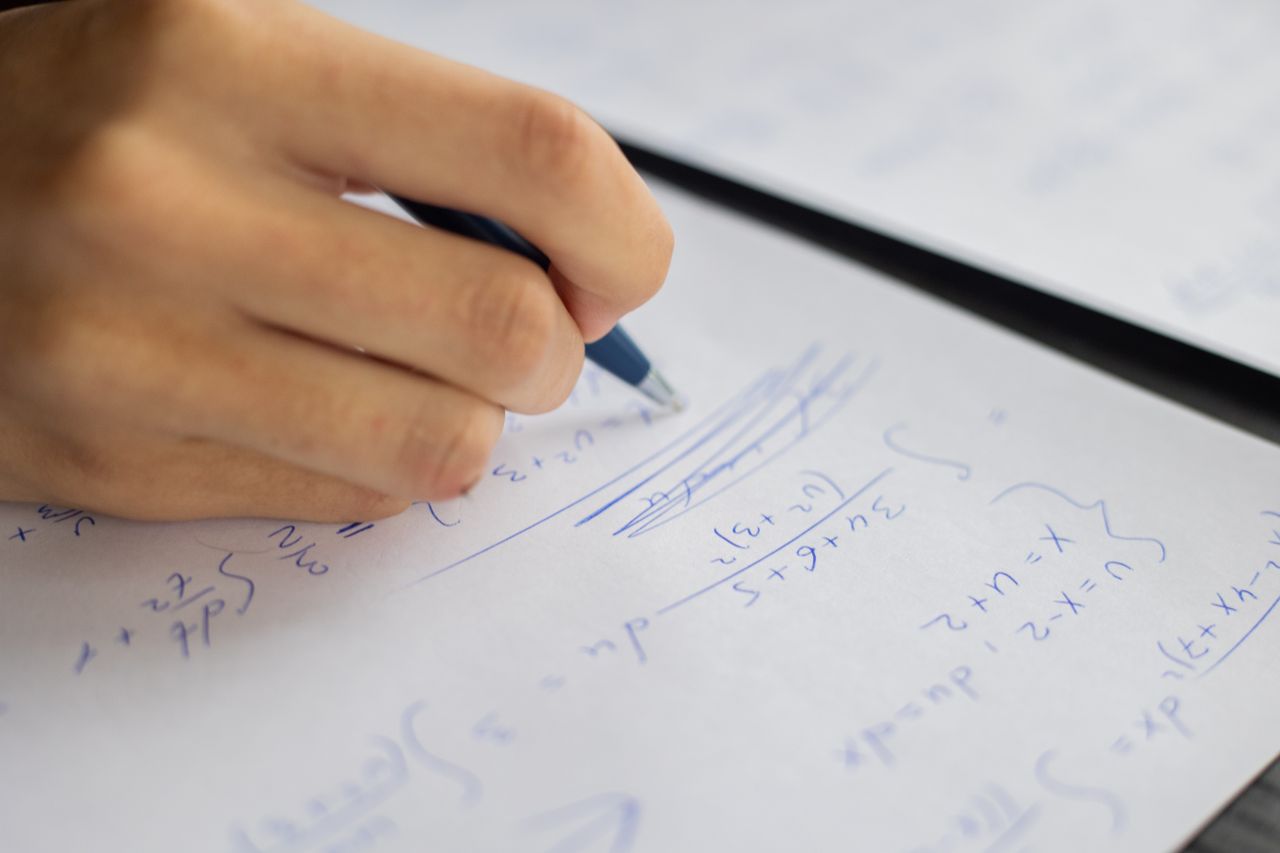 about-01 Unrecognizable smart student taking notes on piece of paper while solving mathematical formulas during lesson in classroom on blurred background