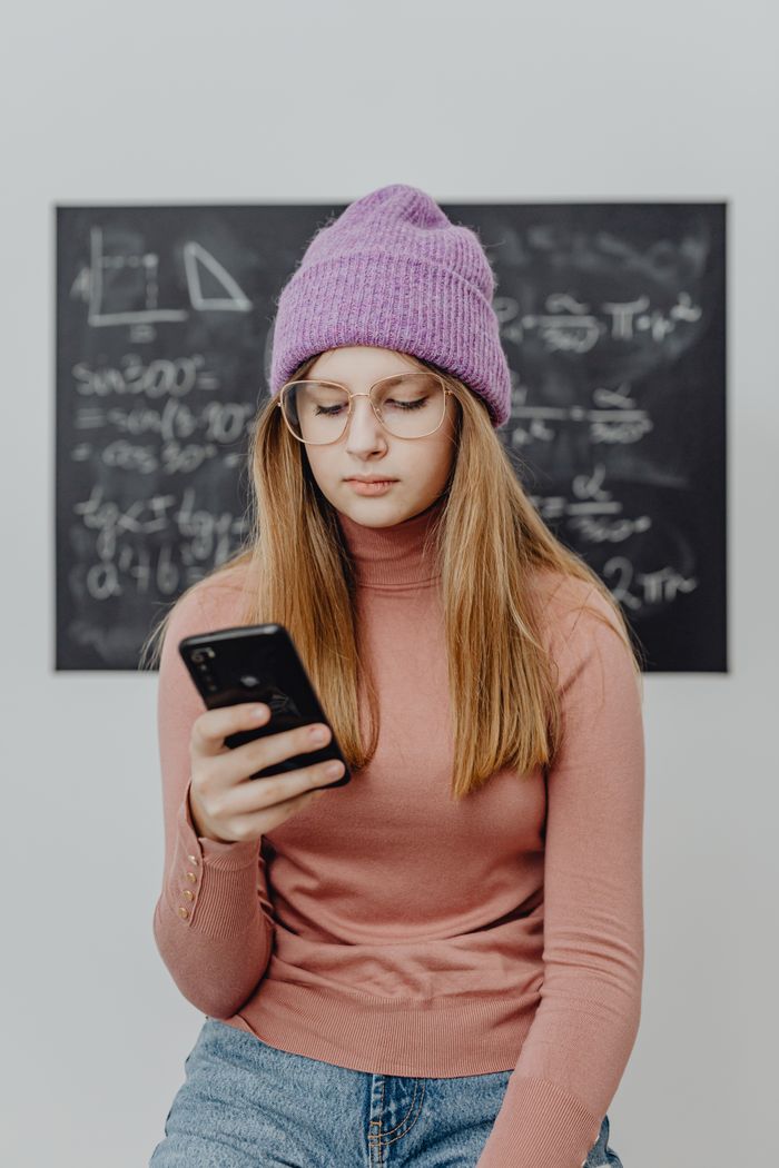 hero-img-01 Young woman engaged in learning using a smartphone in front of a blackboard with math equations.